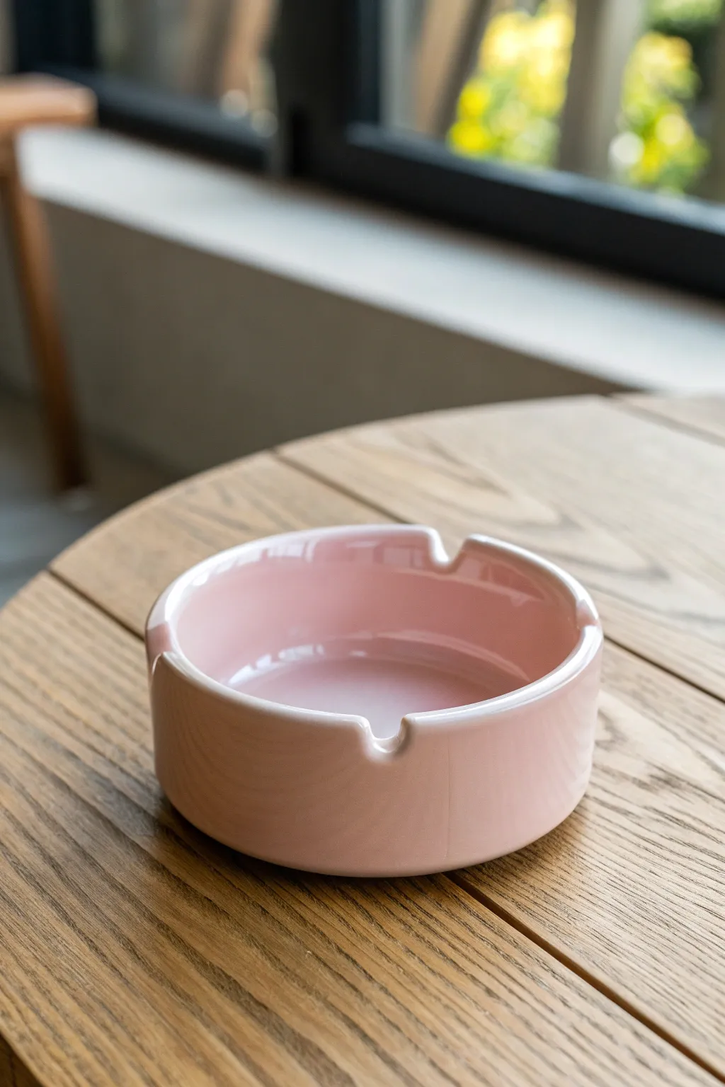 Glossy round ceramic ashtray with clean rim notches, styled on warm wood in soft daylight.