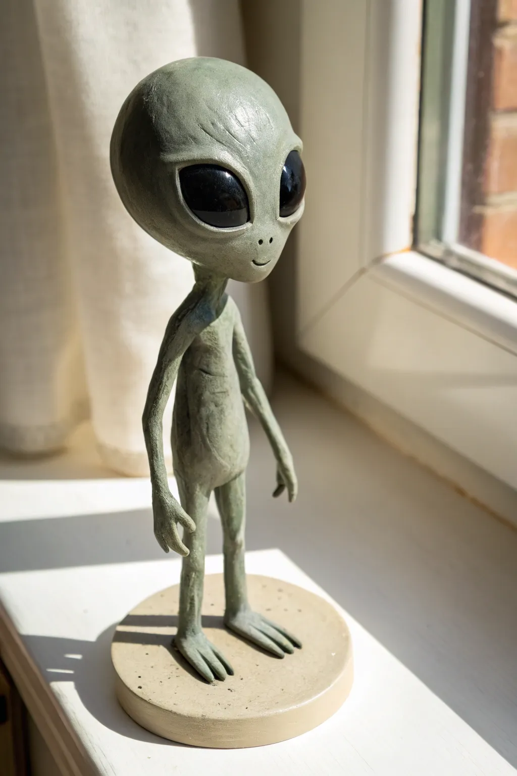 Classic grey clay alien with big black eyes, minimalist styling, soft light, and handmade charm