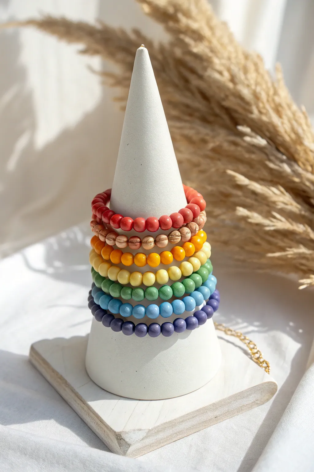 Classic rainbow clay bead bracelet stack on a minimalist cone, clean backdrop for easy color copying
