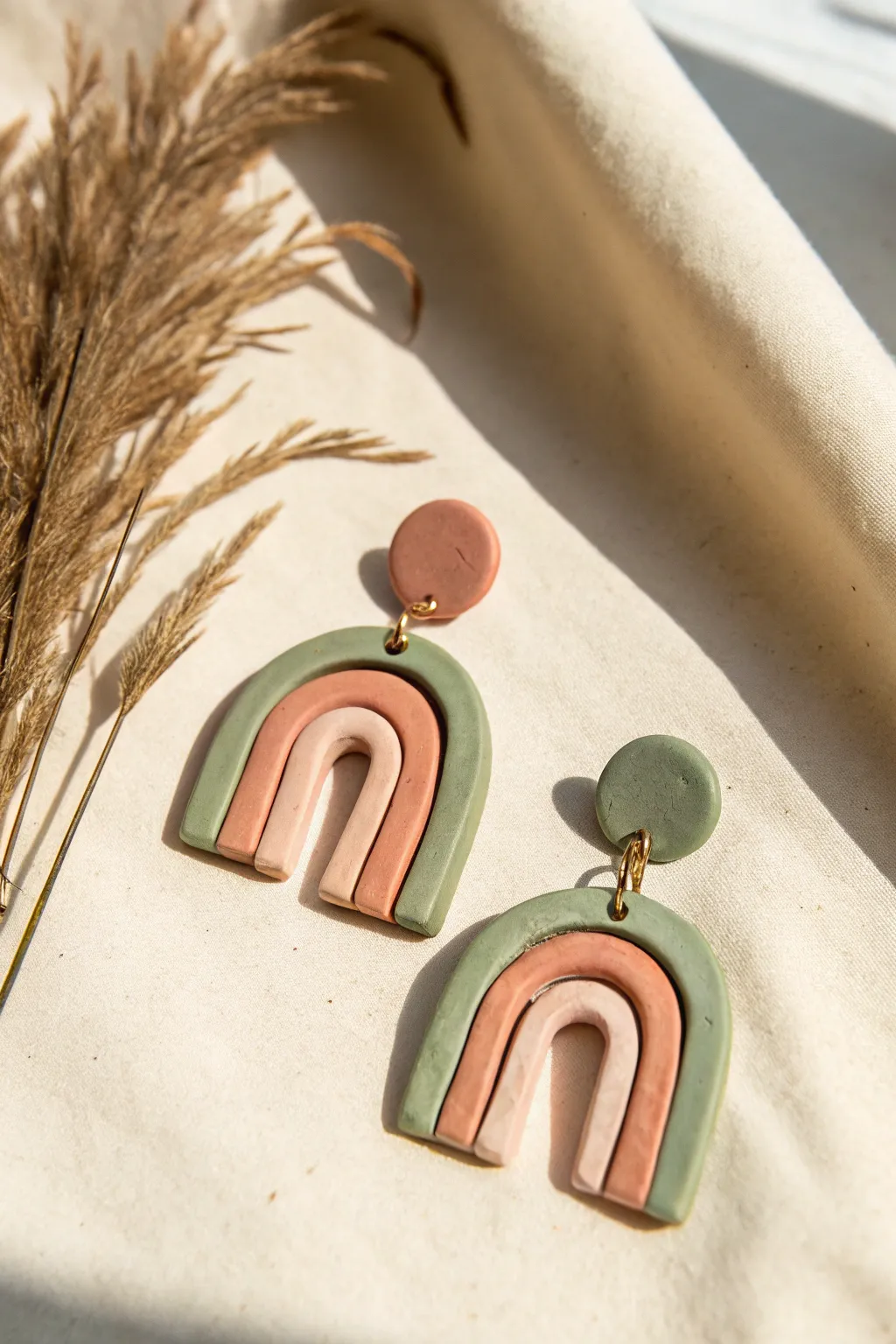 Modern arch and rainbow clay dangles in muted tones, minimalist flatlay with boutique charm.