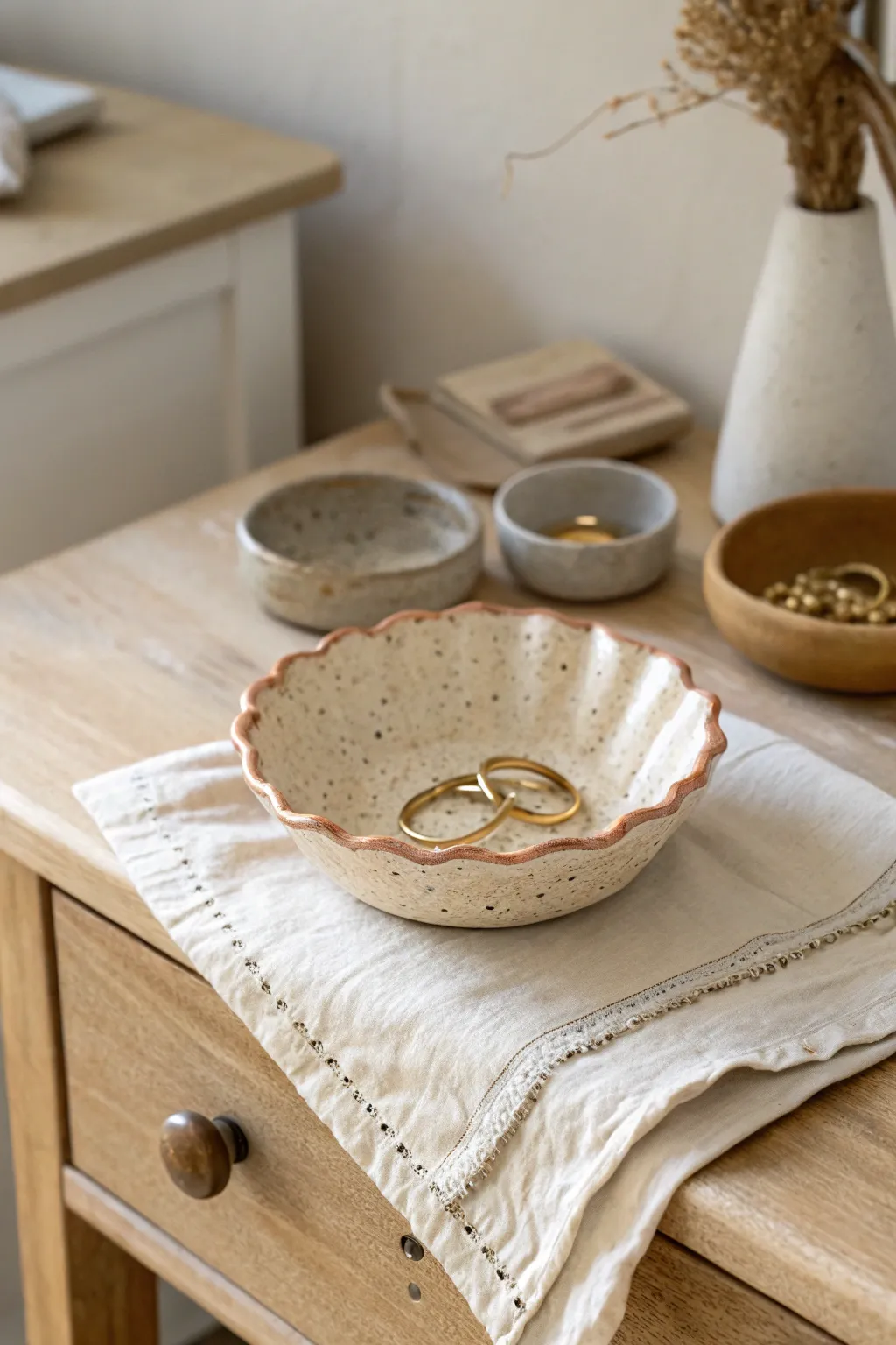 Scalloped clay trinket dish in warm neutrals, styled for rings and hair clips on a nightstand.