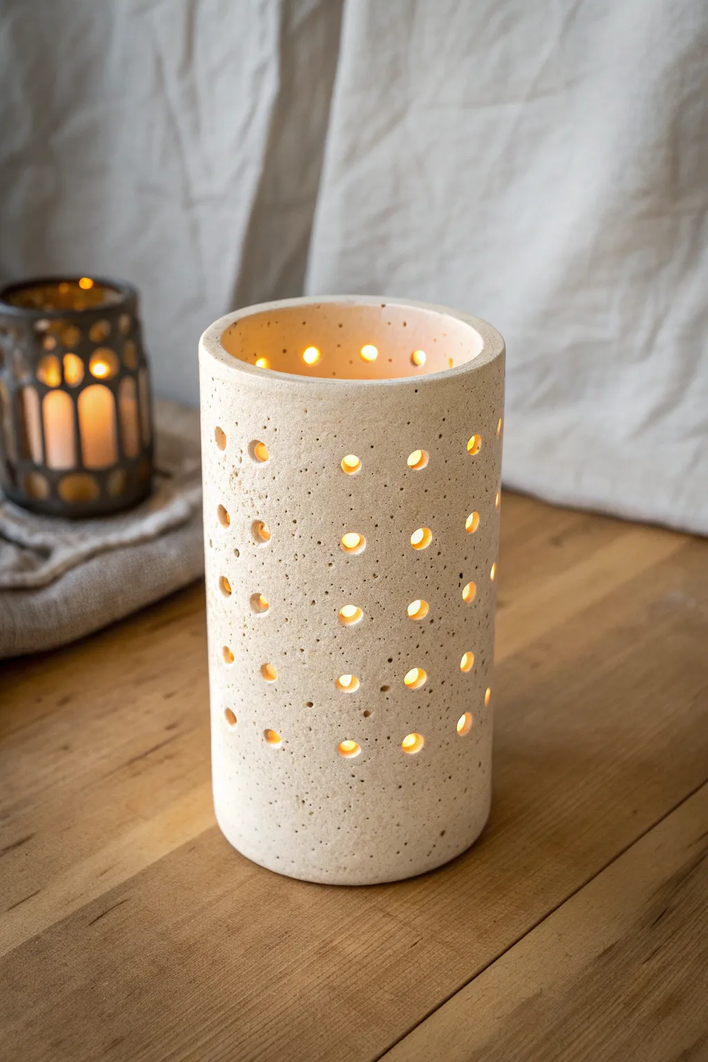Minimal clay cylinder luminary with mixed round cutouts, glowing warmly and casting soft dots.