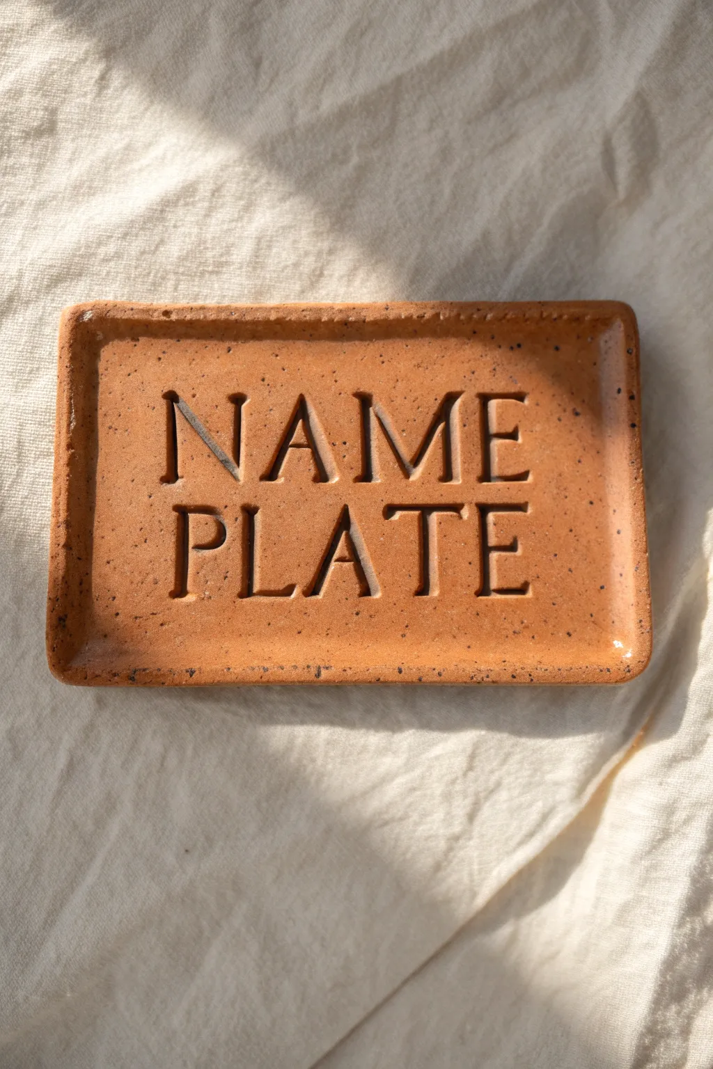 Classic stamped clay name plate in warm terracotta with dark inky impressions, simple and chic