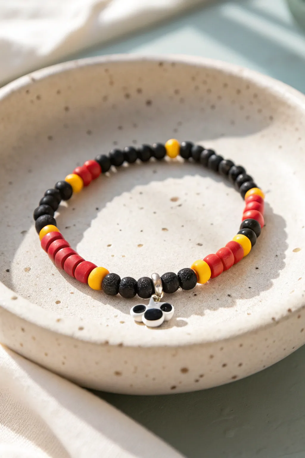 Minimal mouse-ear center bracelet with classic black red yellow heishi beads on a neutral dish