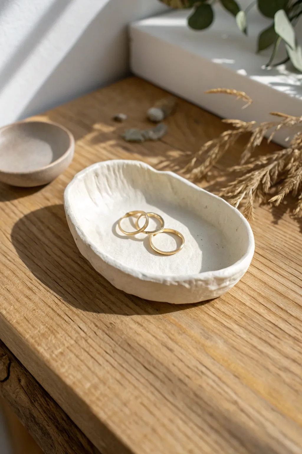 Minimal air-dry clay trinket dish with pinched edges, styled in warm neutrals on light wood