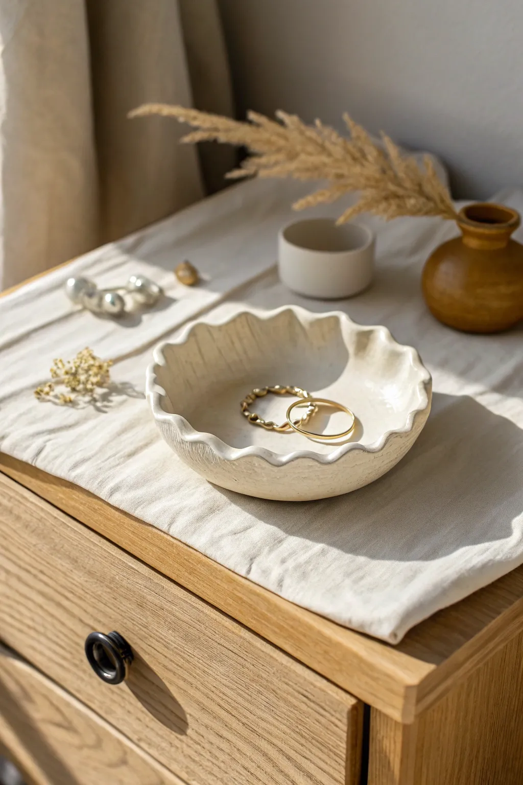 A simple wavy air-dry clay trinket dish, styled for rings and earrings on a cozy nightstand.