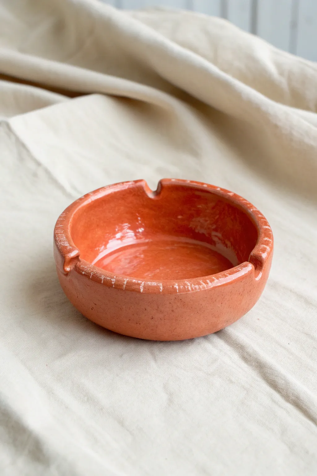 Classic pinch pot ashtray in glossy coral, minimalist and handmade with two simple rim notches.