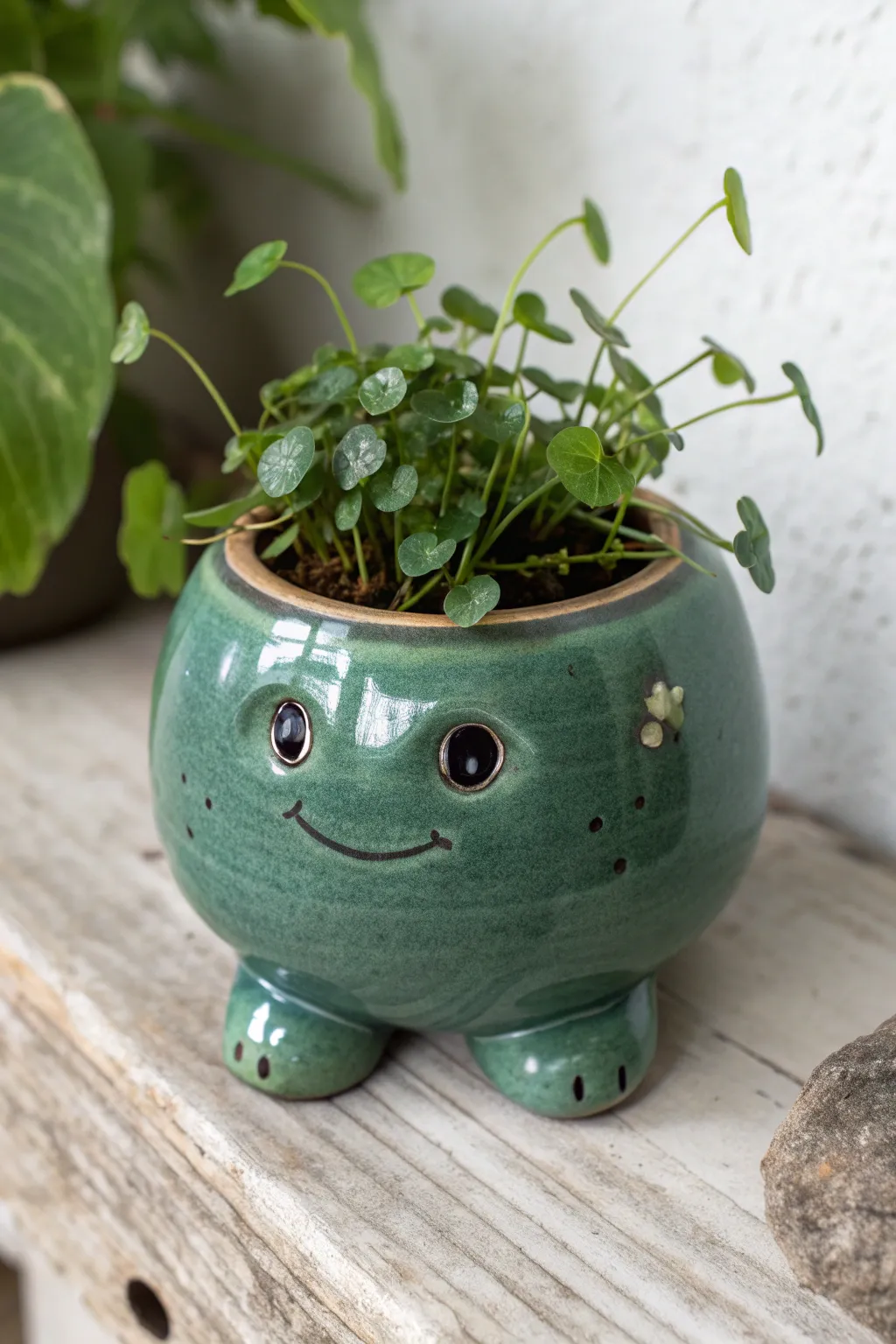 Playful glossy green frog planter with dangling legs and leafy hair, simple and charming.