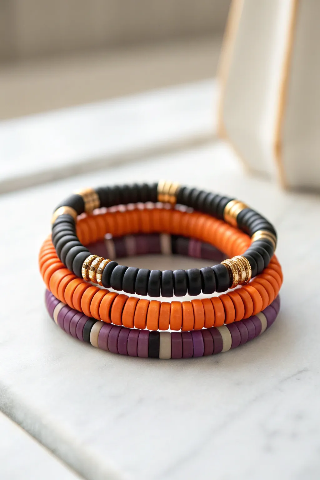 Classic Halloween heishi bracelet stack in orange, black, and purple on a bright minimal backdrop.