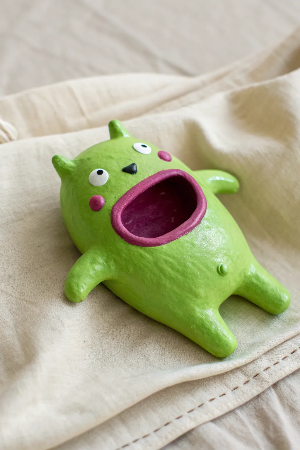 Bright green pinch pot monster with a bold gaping mouth, simple eyes, and cozy handmade charm.