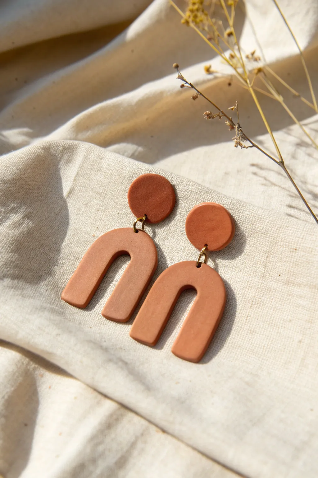 Simple cutout polymer clay dangle earrings in arches and circles on natural linen.