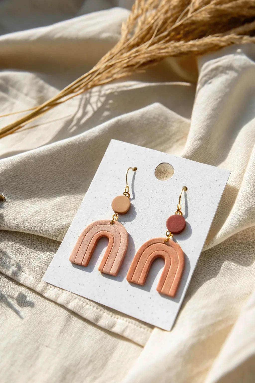Modern polymer clay arch earrings in soft earthy tones, styled simply on linen for a clean look