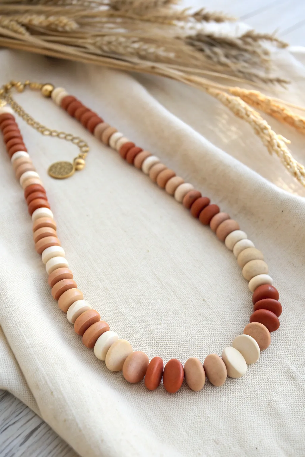 Simple polymer clay disc bead necklace in warm neutrals, clean flat lay, boho minimal vibe.