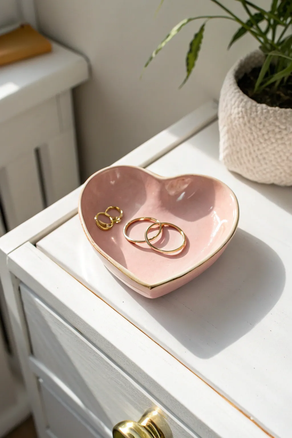 Blush heart trinket dish with glossy shine, perfect for rings and tiny hoops on a white nightstand.