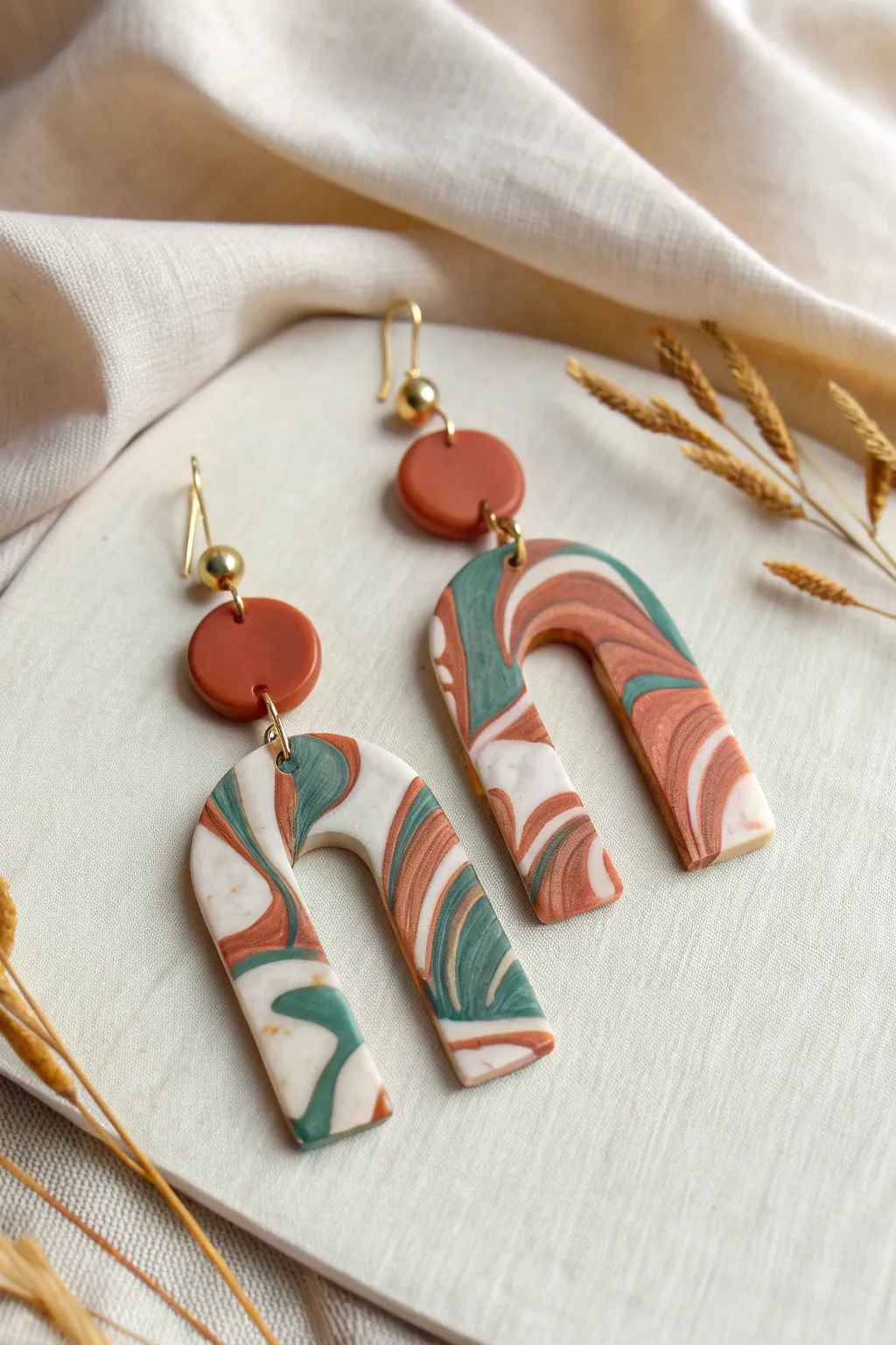Bold marbled polymer clay dangle earrings in easy arch shapes on a clean neutral backdrop