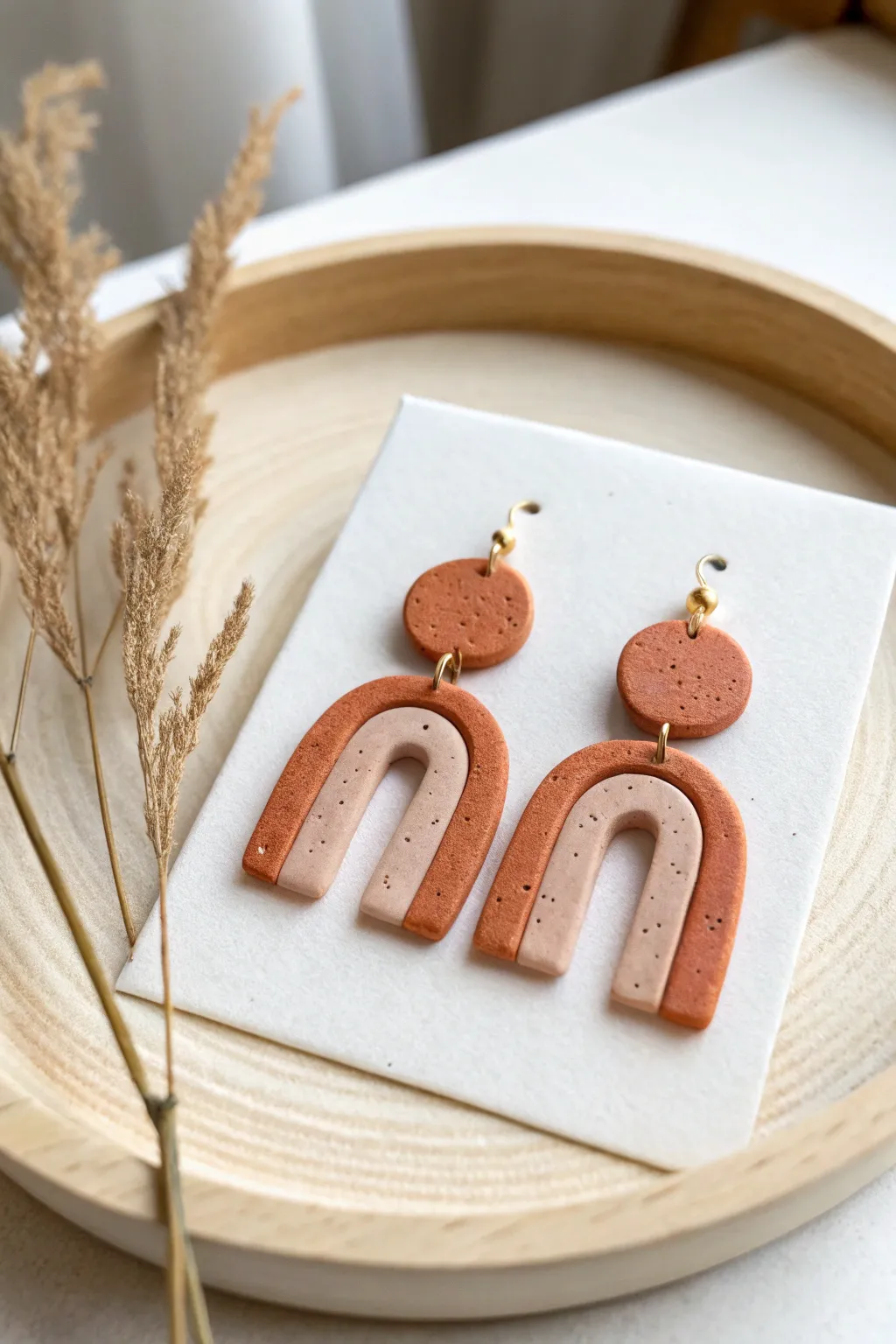 Minimal arch and dangle oven-bake clay earrings in two tones, styled clean and bright