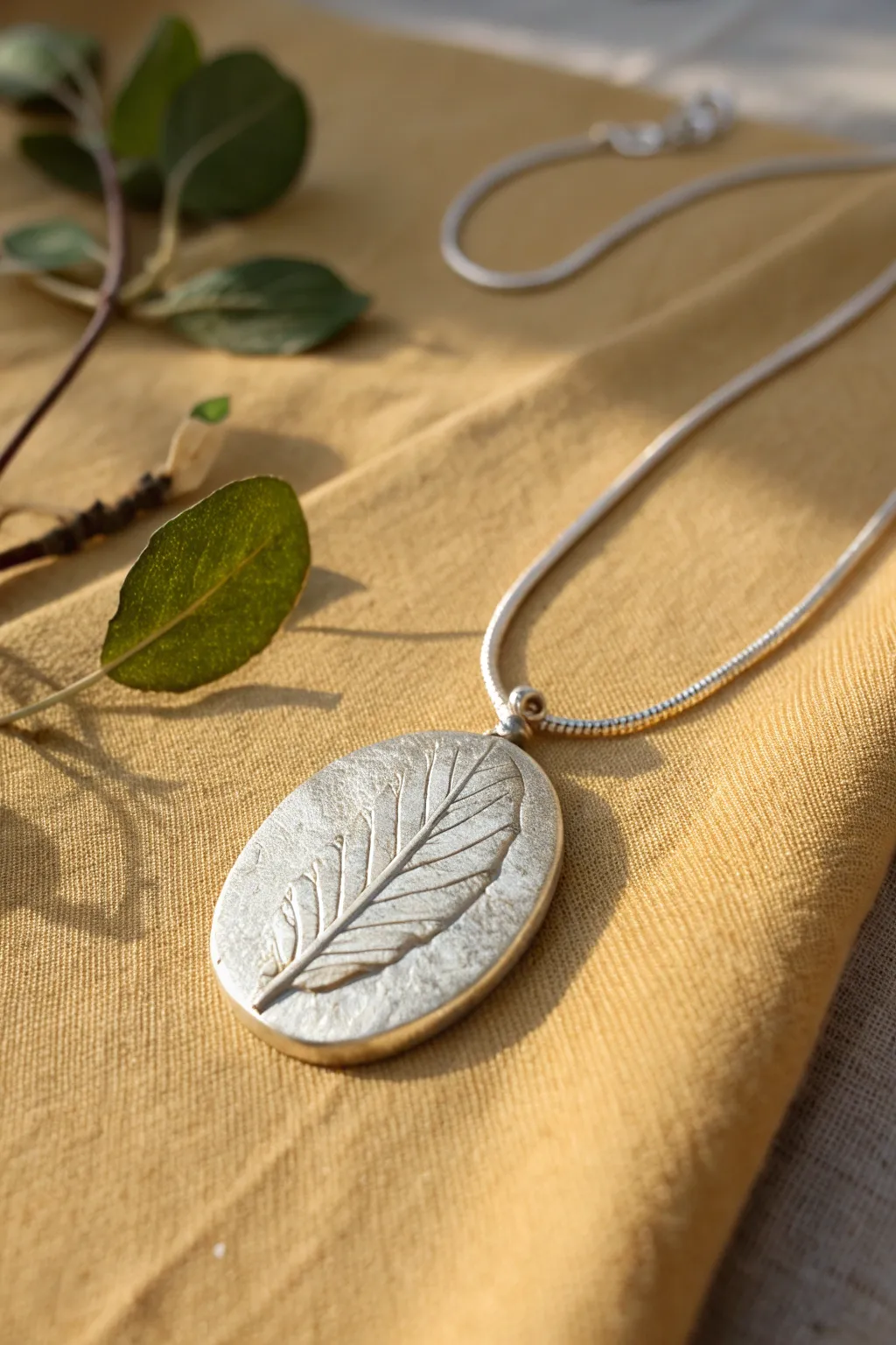 Minimal silver clay leaf pendant with crisp vein imprint, styled beside its real leaf muse