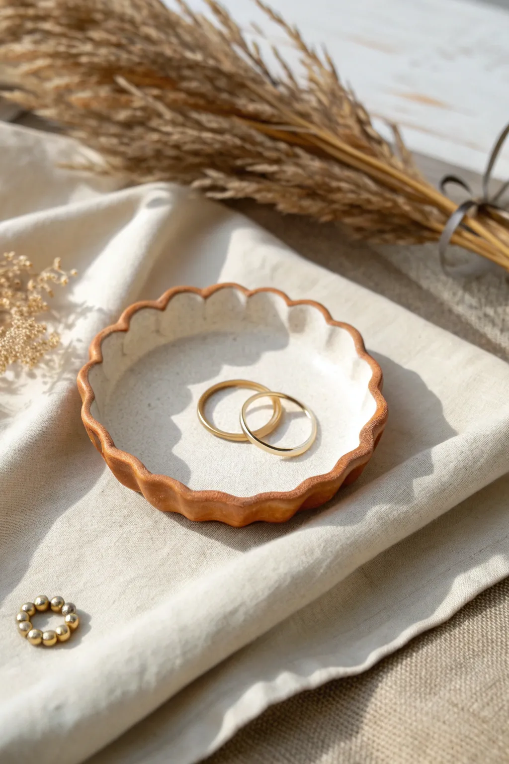 Tiny scalloped ring dish in soft clay tones, styled with simple jewelry on linen.