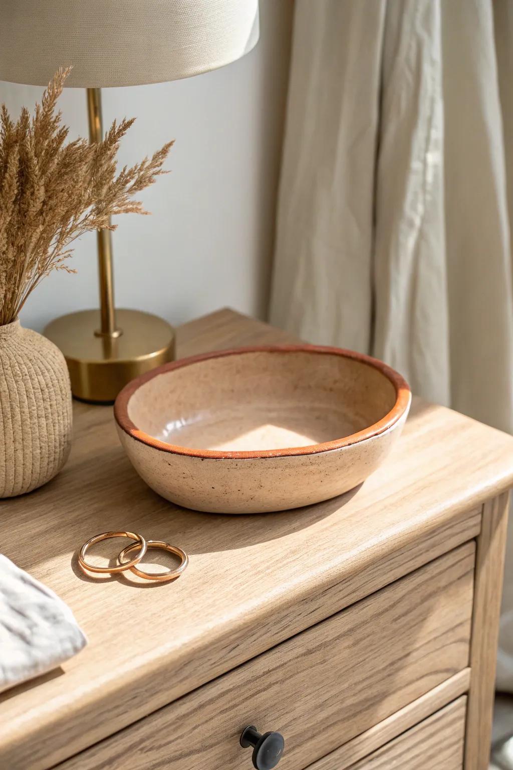 Mini handmade trinket dish in soft neutrals with a muted terracotta rim, styled by rings.