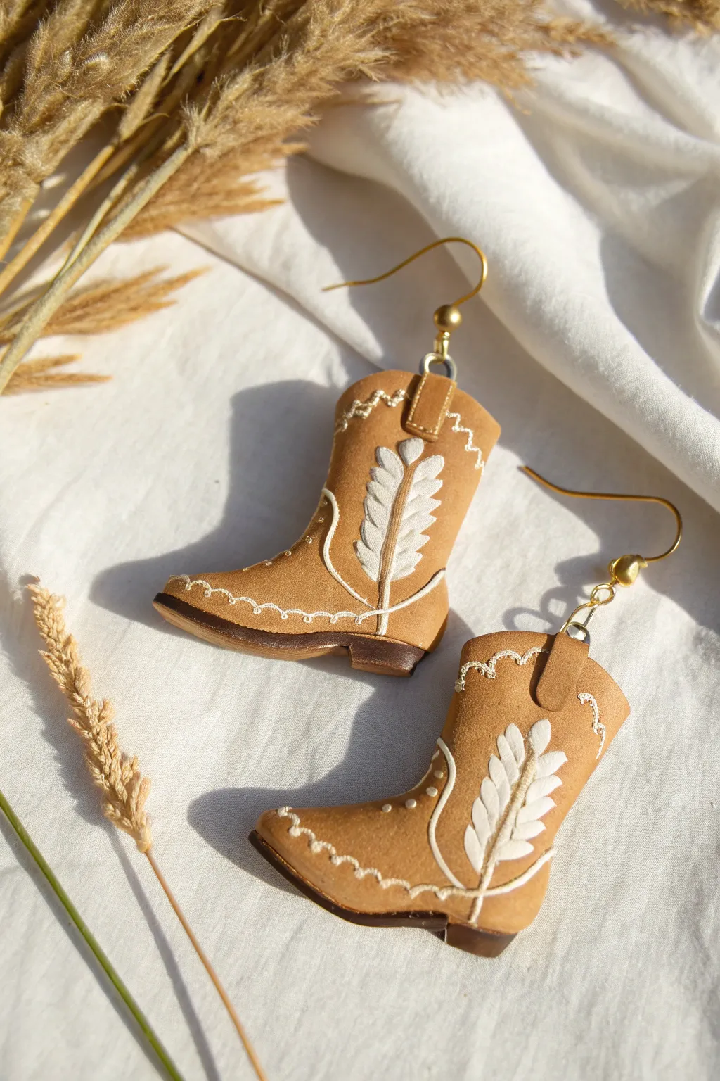 Warm tan cowboy boot dangle earrings with simple stitches, minimalist boho Western charm.