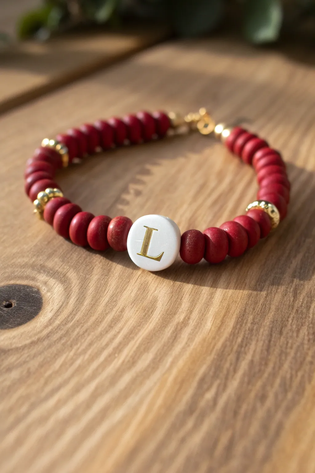 Scarlet clay beads with gold spacers and a single L charm, styled on warm wood for cozy magic.