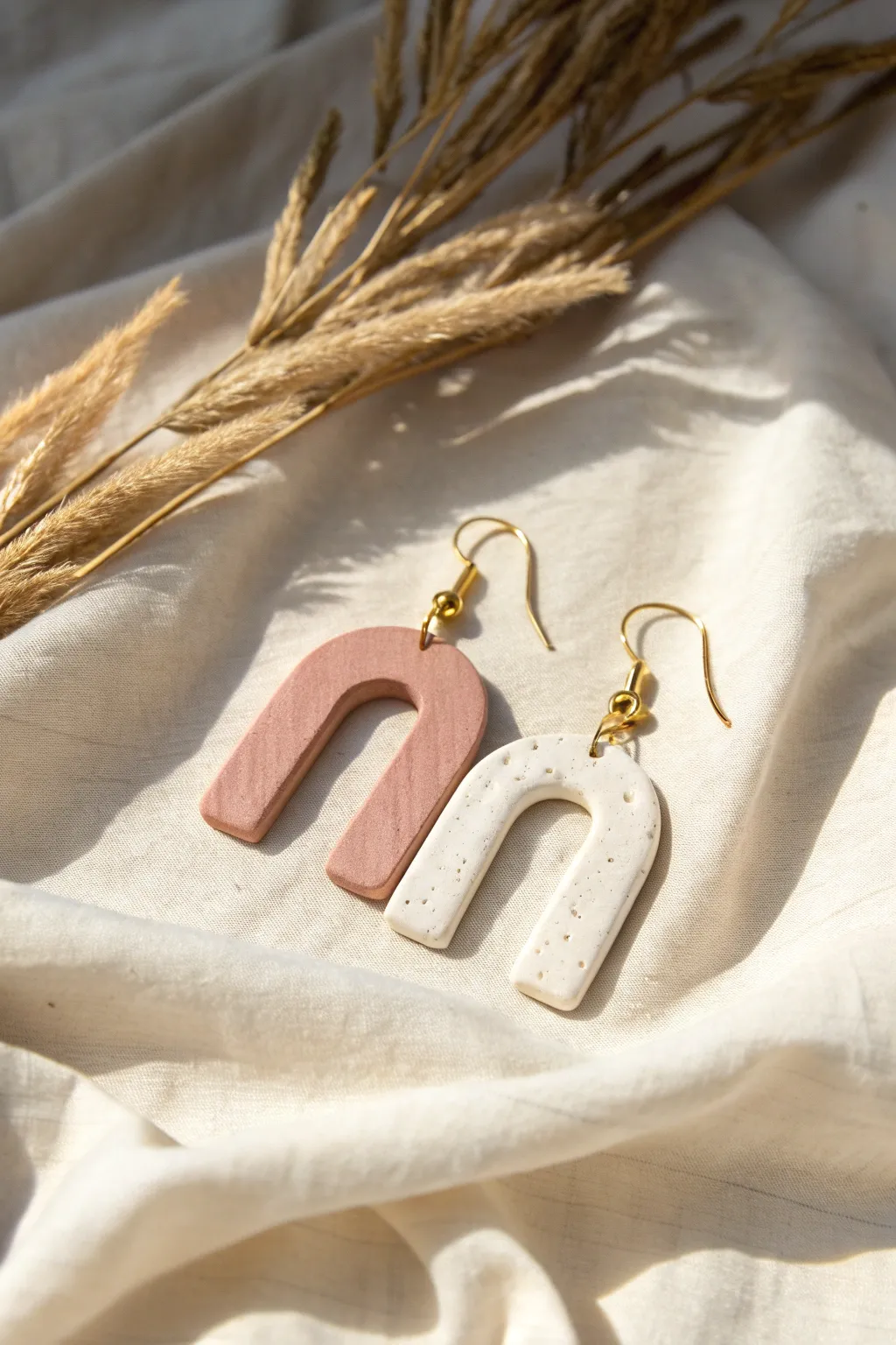 Muted pink and warm white abstract arch earrings on linen, minimal boho and softly sunlit.
