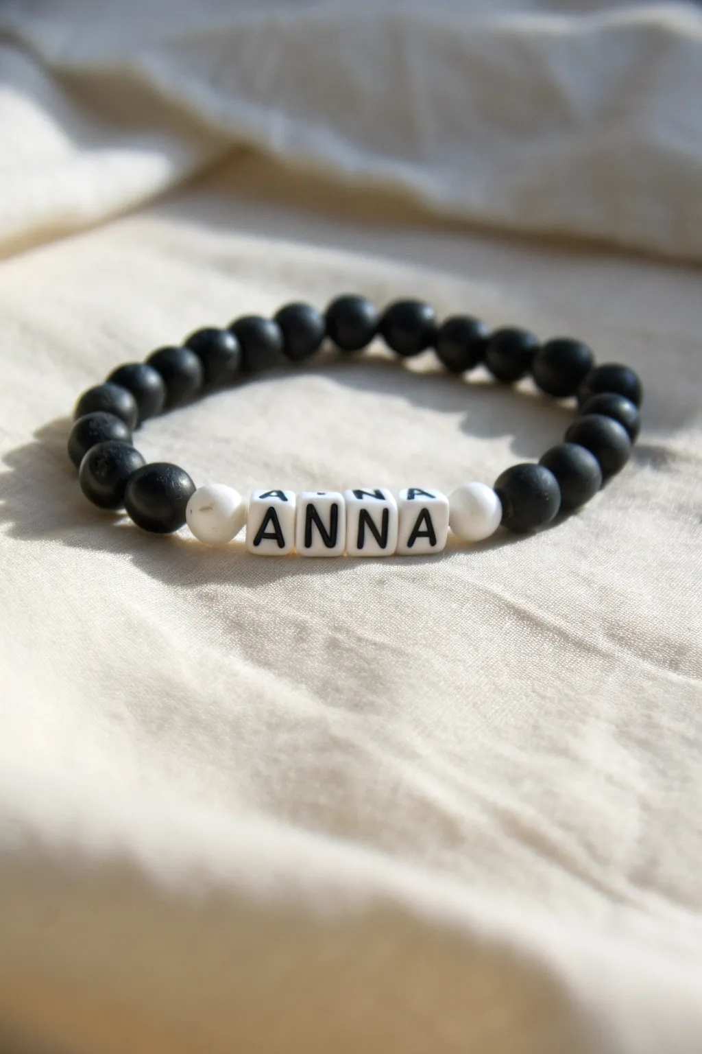 Monochrome clay bead bracelet with a letter-bead name center, minimal Scandinavian charm.