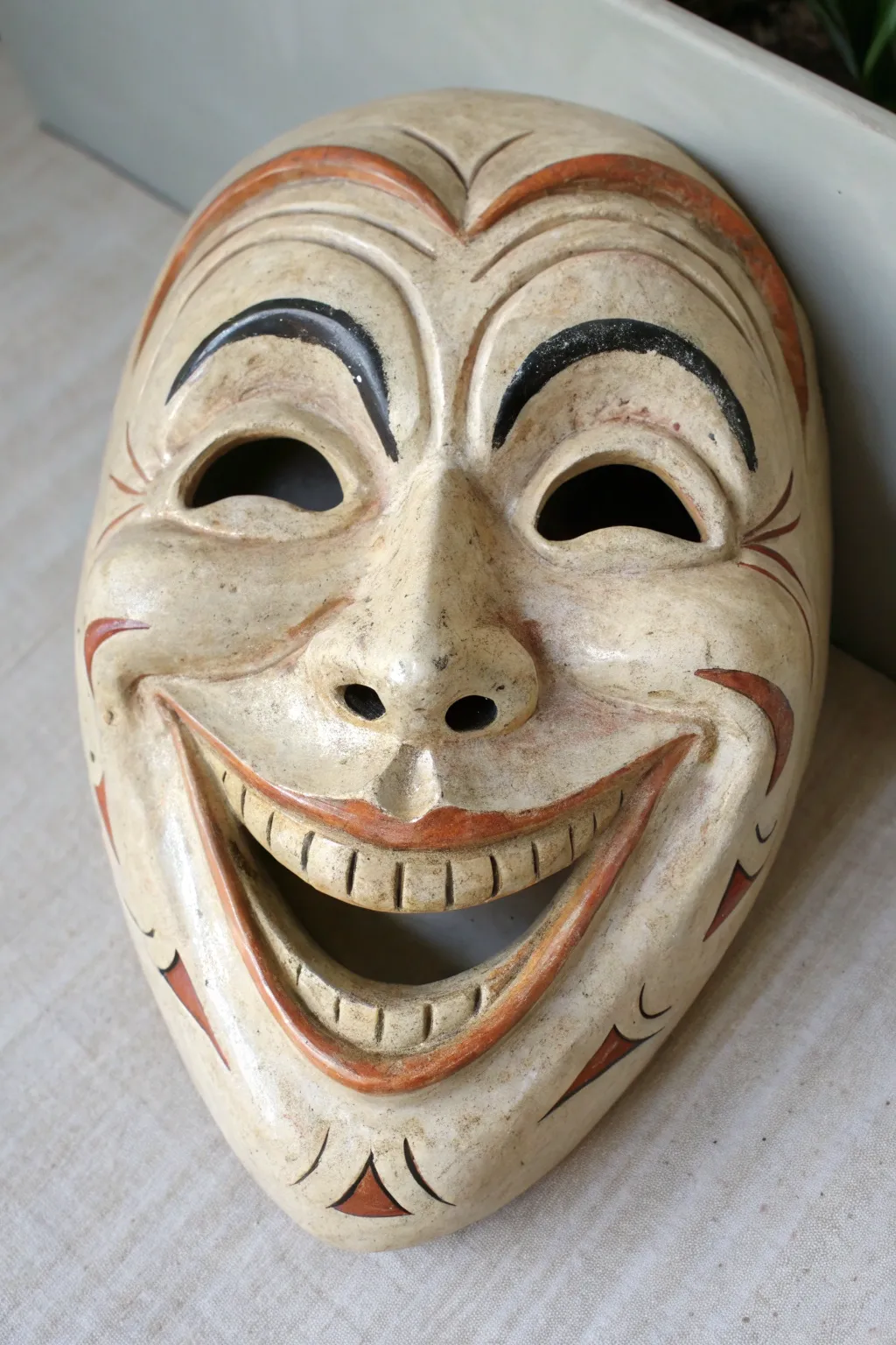 Playful grinning jester clay mask with bold color blocks, minimal styling, high contrast.