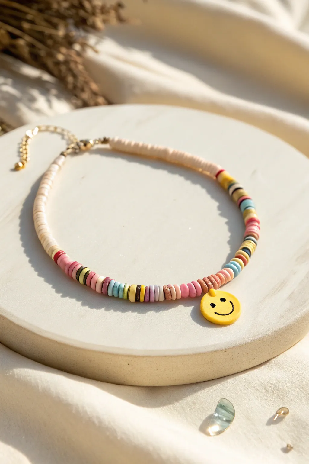 Pastel heishi clay bead anklet with a tiny smiley centerpiece for a playful minimalist look.