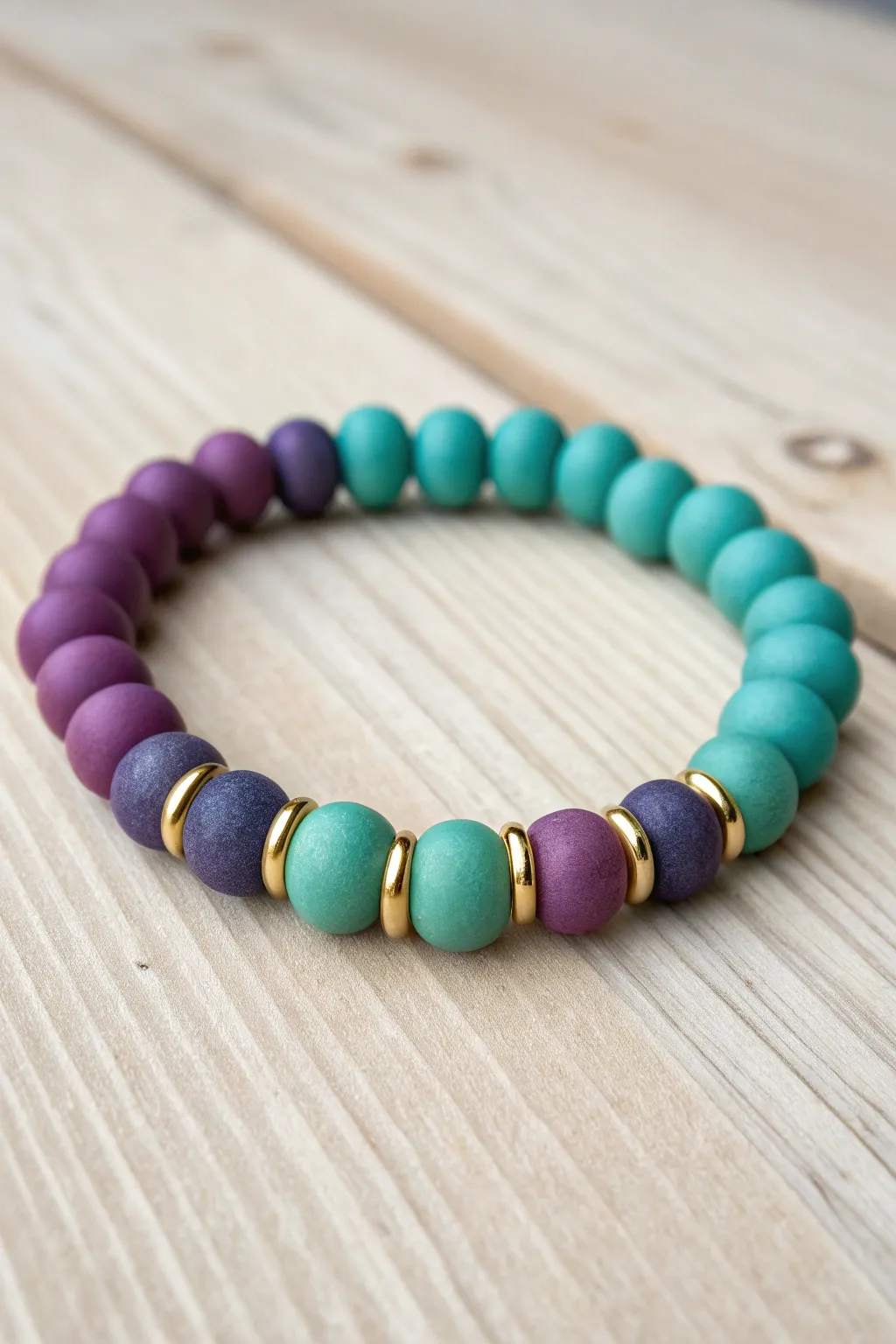 A purple-to-teal clay bead bracelet with glossy metallic spacers and zero white beads anywhere.