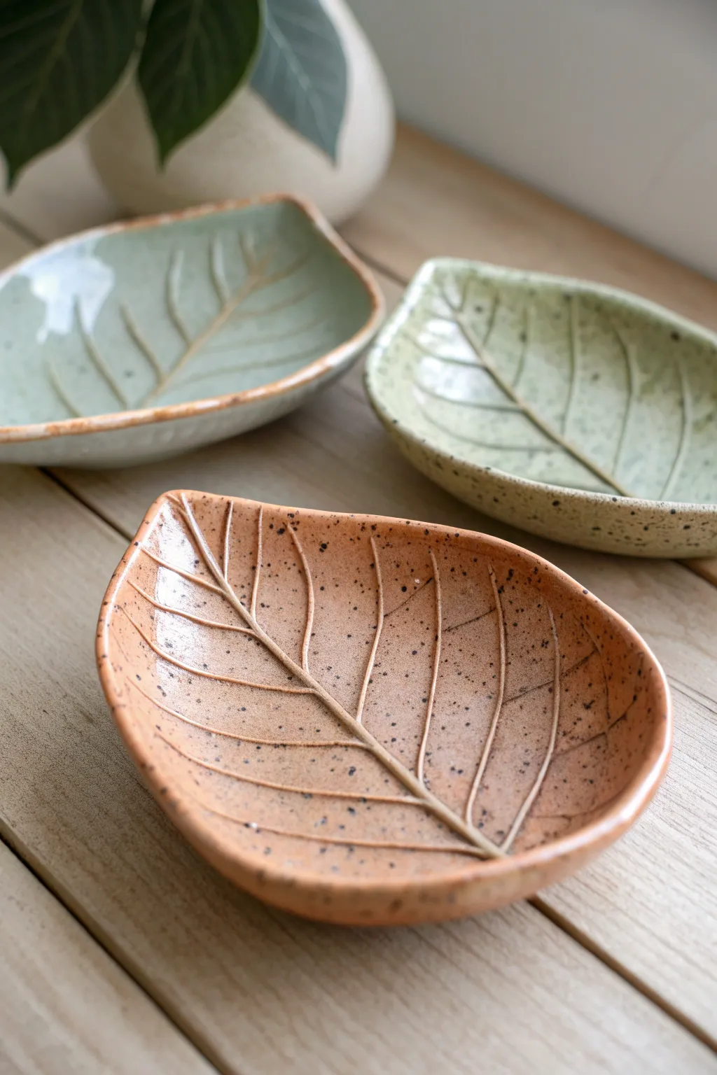 Minimal leaf-imprint trinket plates in earthy tones, styled on light oak for calm boho contrast.