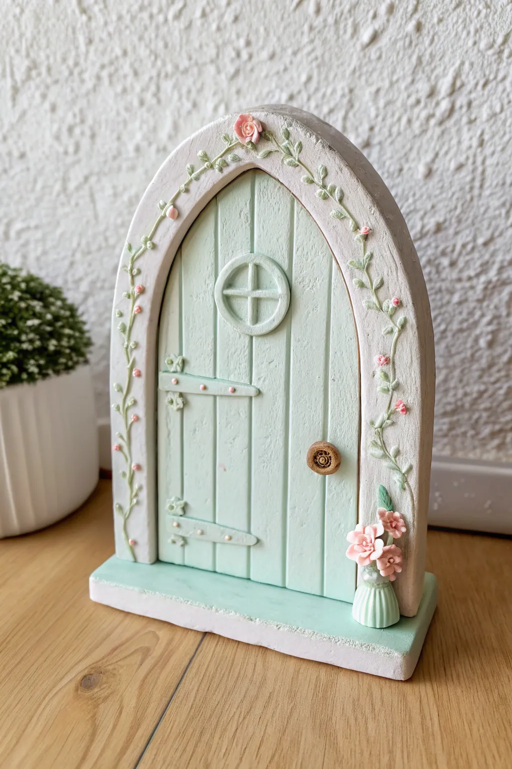 Soft pastel clay fairy door with simple panel lines and a tiny vine for cottage charm.