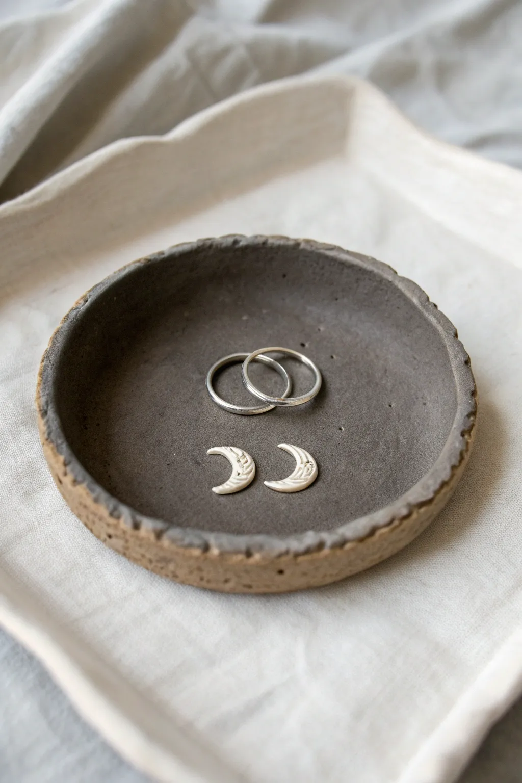 Minimal moon phase clay dish in matte charcoal, styled with silver rings for a celestial look