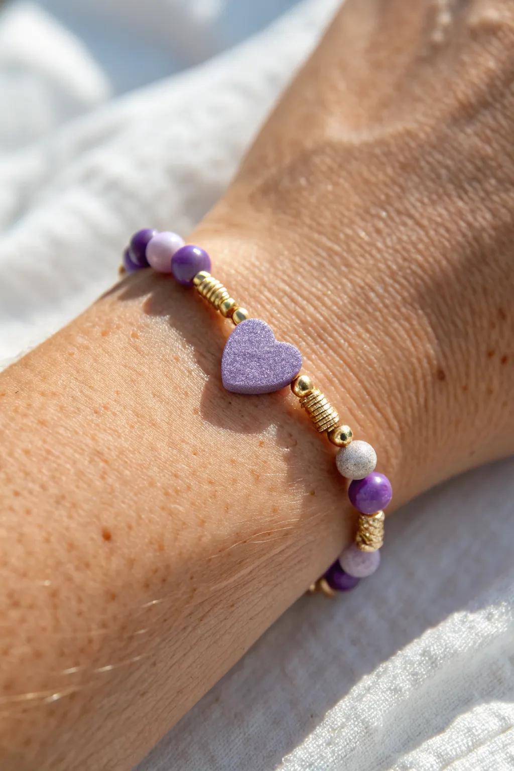 Tiny purple heart centerpiece bracelet with gold spacers, minimalist and sweet on-wrist.