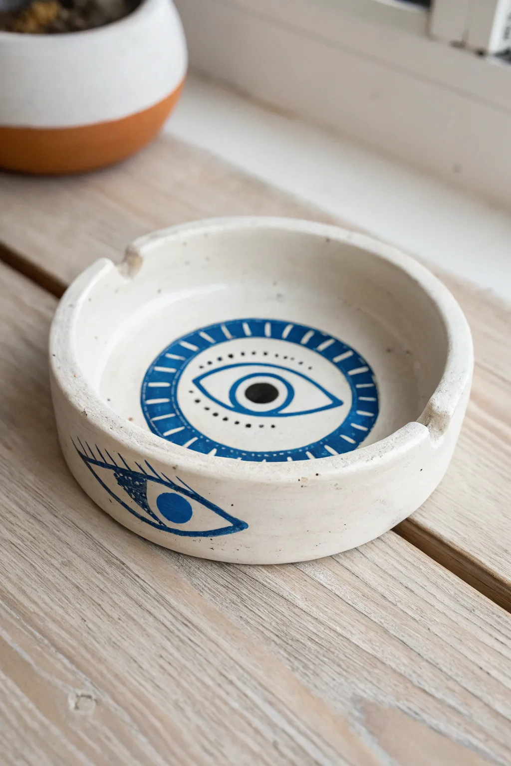 Minimal round clay ashtray with a bold blue evil eye motif, glossy finish, and clean Nordic style.