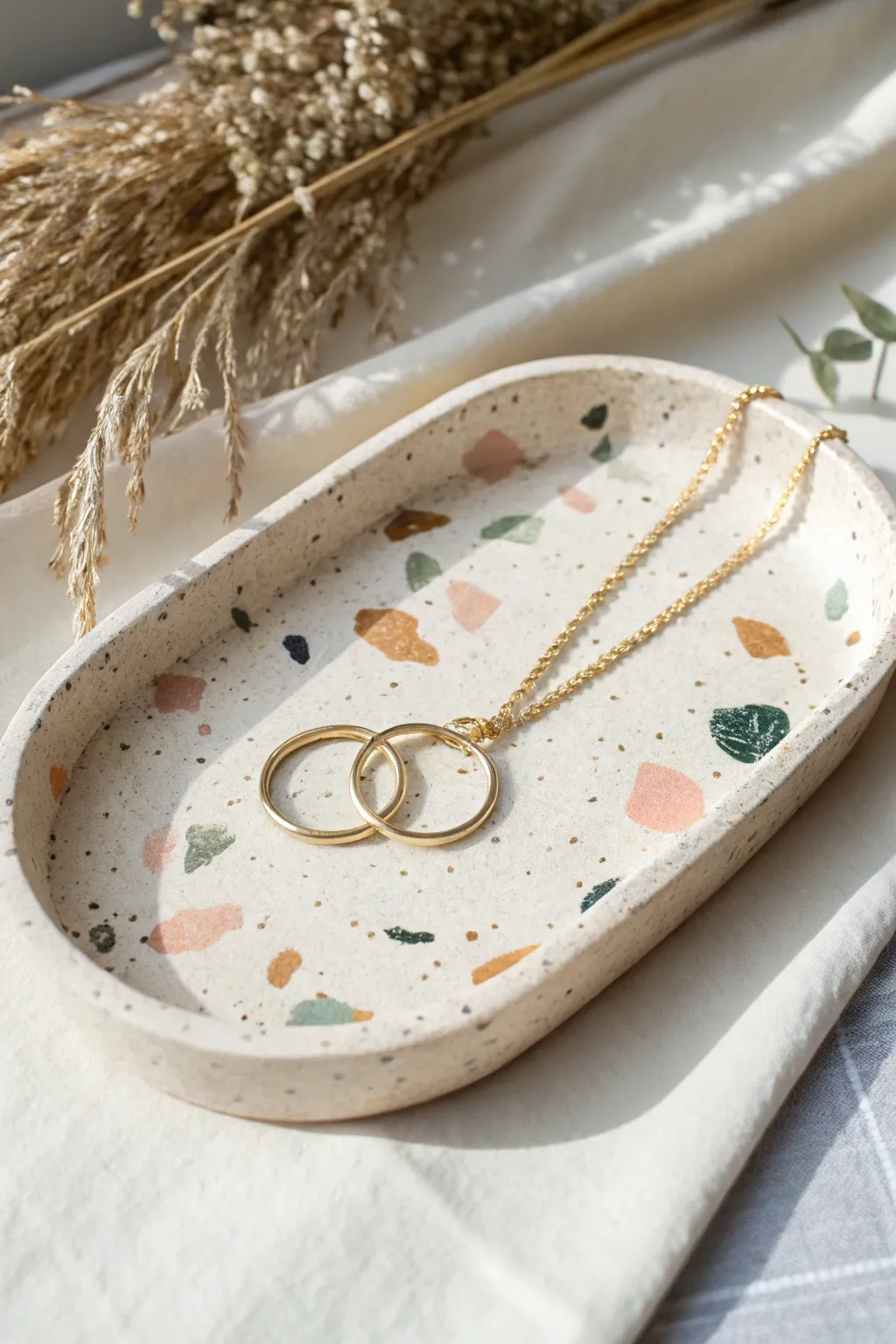 Minimal terrazzo clay jewelry tray with soft speckles, styled with rings and a delicate chain.