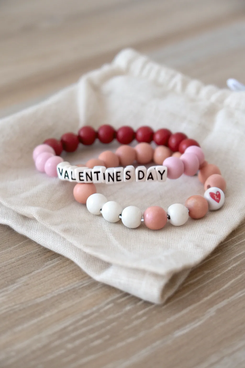 Matching initials and heart clay bead couple bracelets in blush, red, and white, minimalist boho vibe.