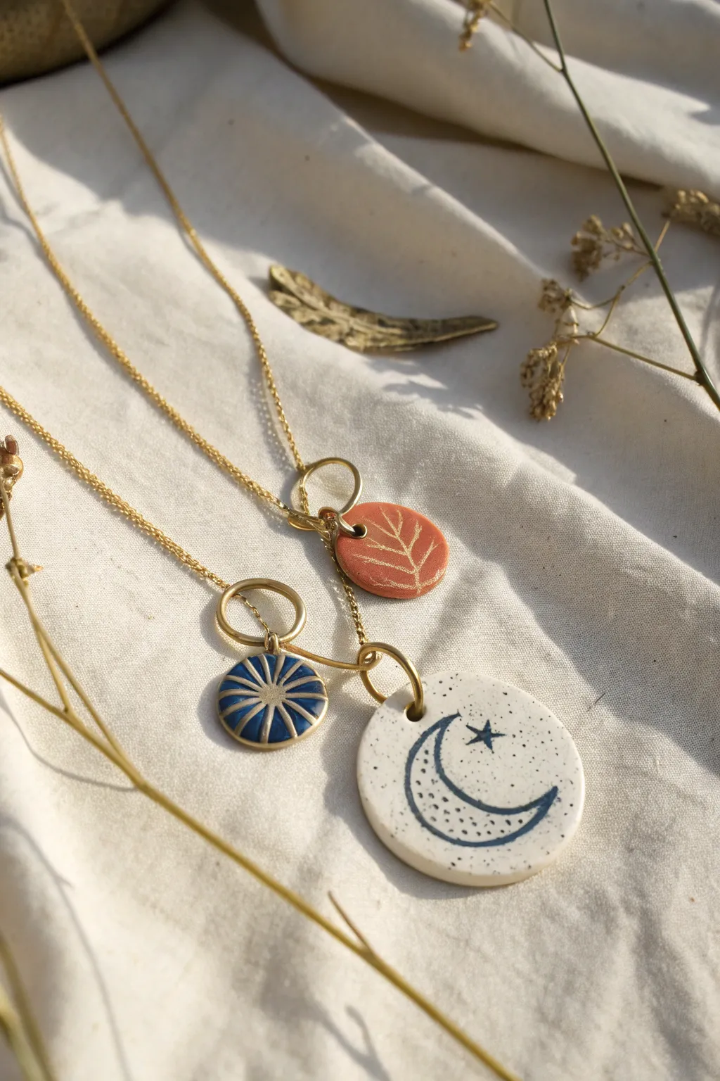 Layered air dry clay charm necklaces in moon and tag shapes, minimalist boho flat-lay on linen.