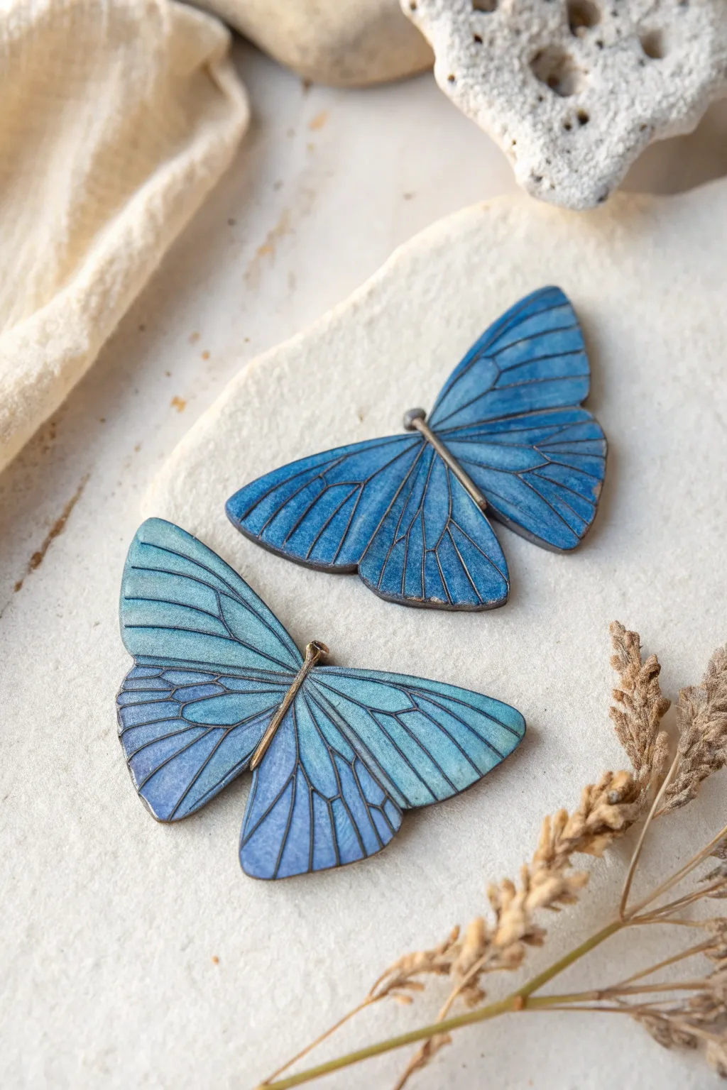 Minimalist cobalt blue butterfly wing pins with delicate veining, styled symmetrically on linen.