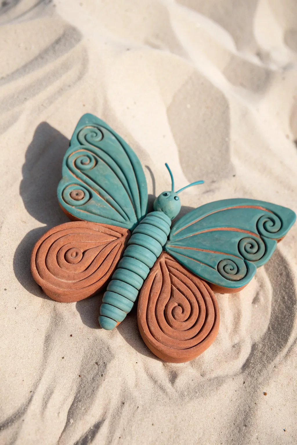 Minimalist clay butterfly with coiled body segments in bold teal and warm terracotta.