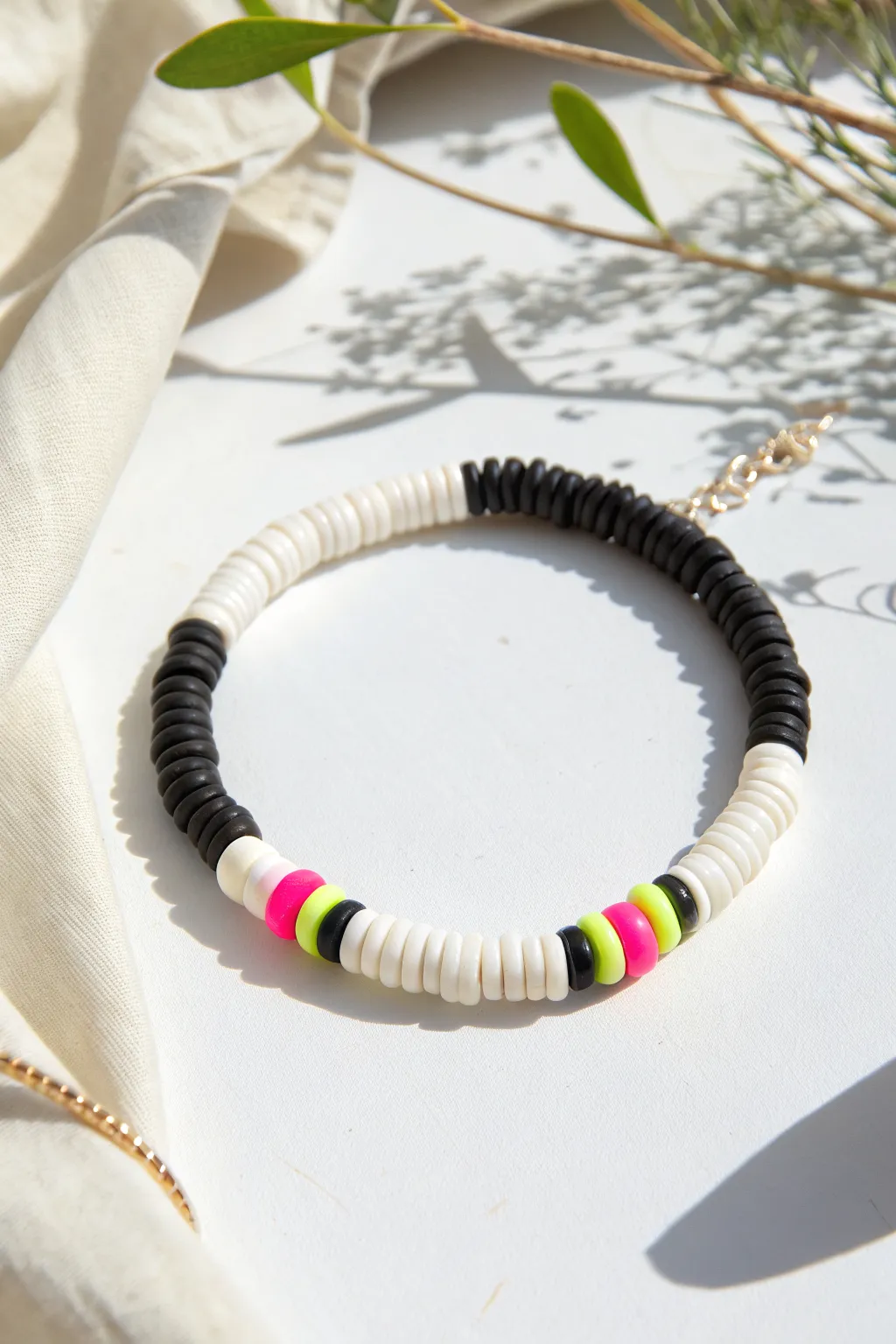 Black and white clay heishi bracelet with a bold neon center pop, clean minimalist flat-lay.