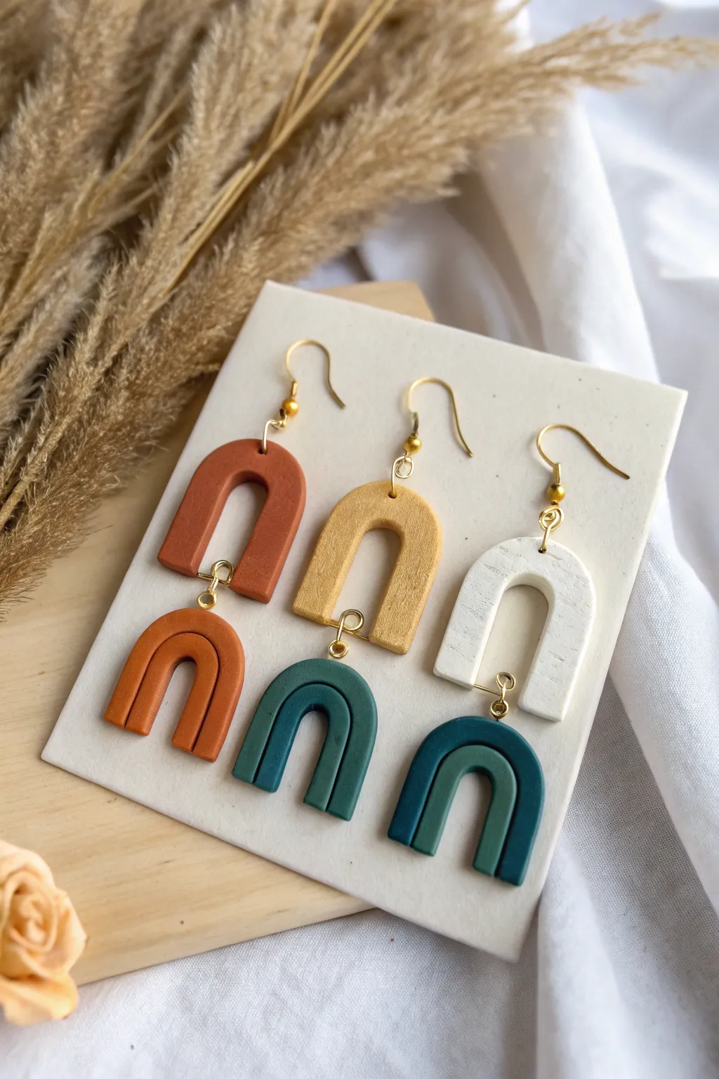 Bold polymer clay arch earrings with marbling and color blocking on a minimalist stand