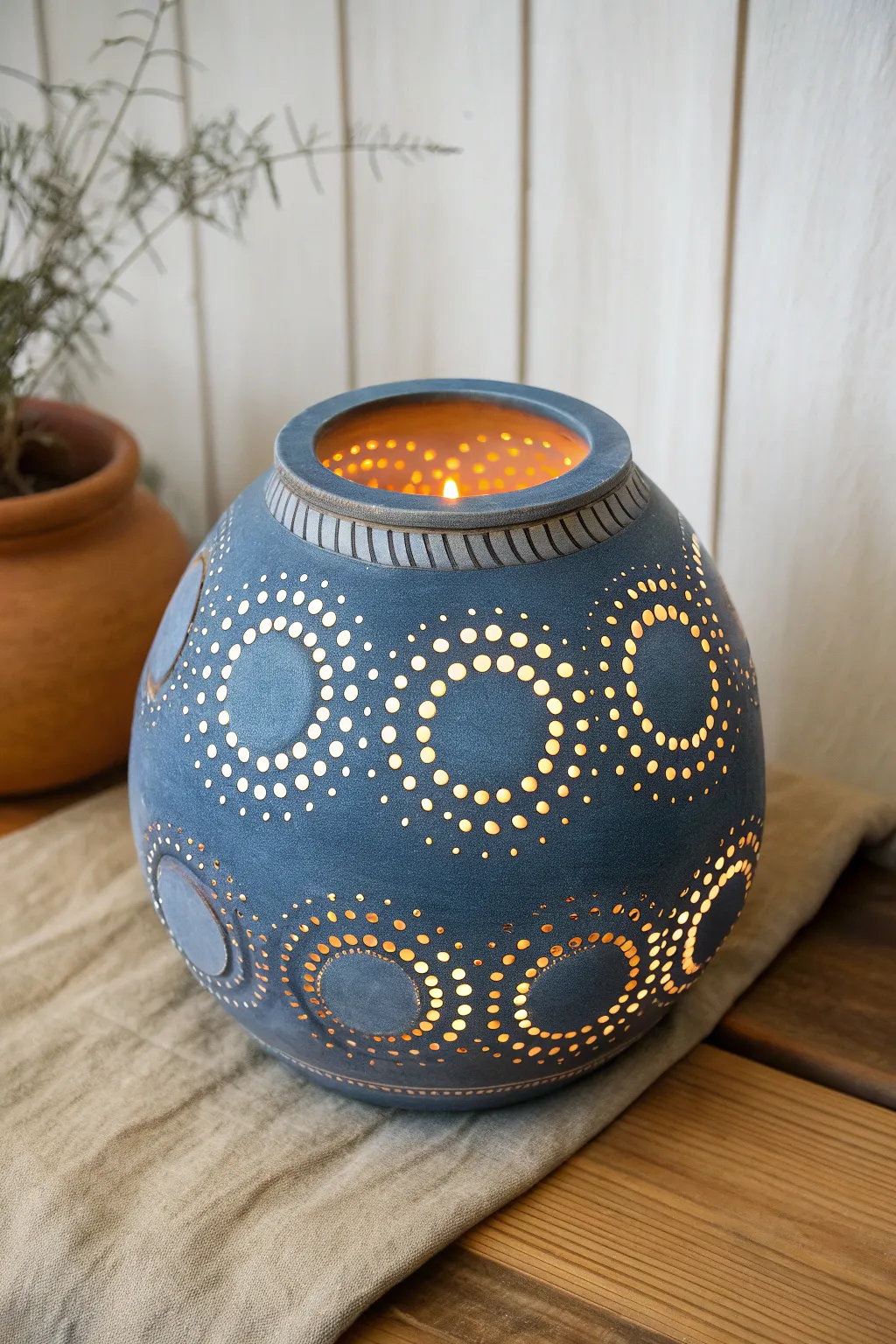 Softly glowing pierced clay luminary, minimalist form with warm light and bold indigo glaze.