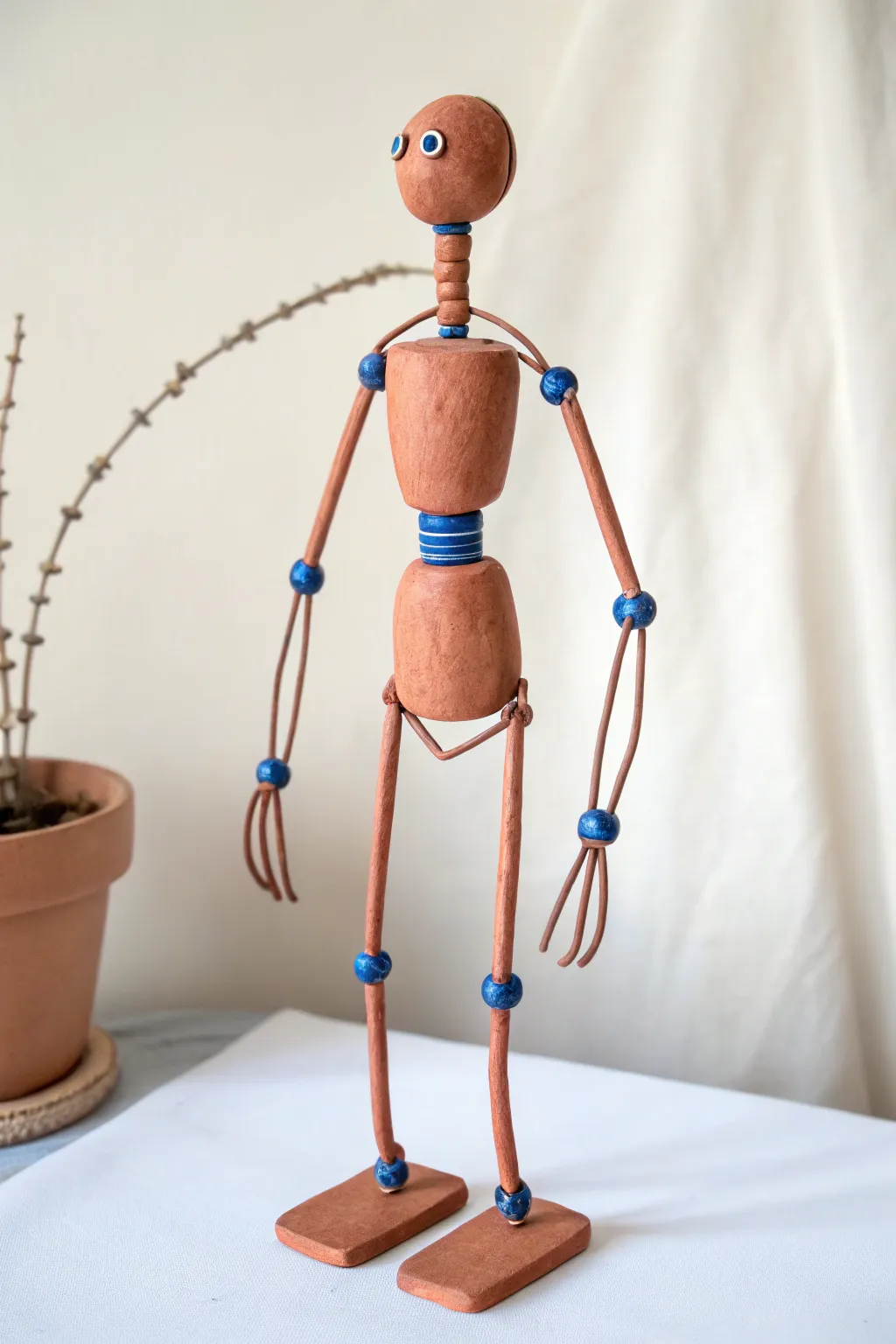 Long limbed clay robot with simple joints and a bold color accent, minimalist handmade charm