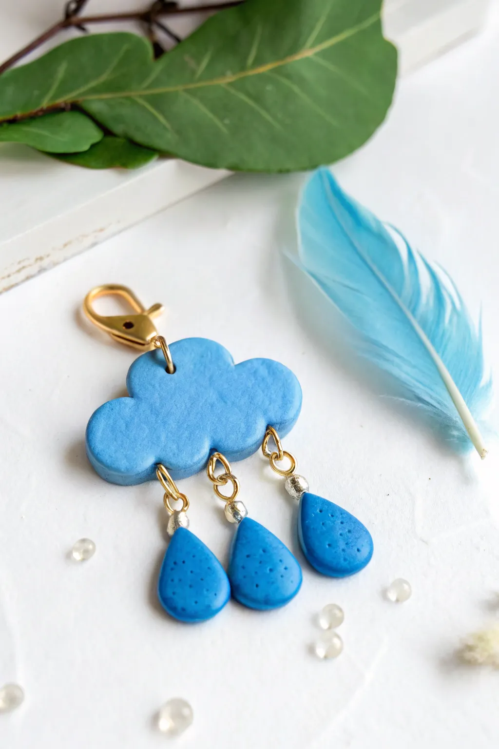 Puffy blue clay cloud charm with matching raindrop dangles, minimalist and bold on white