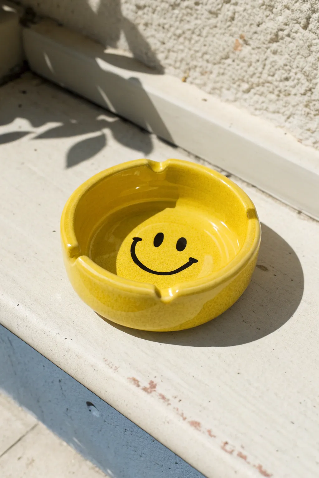 Glossy sunshine-yellow smiley ashtray with clean notches, minimal yet bold pop-art charm.