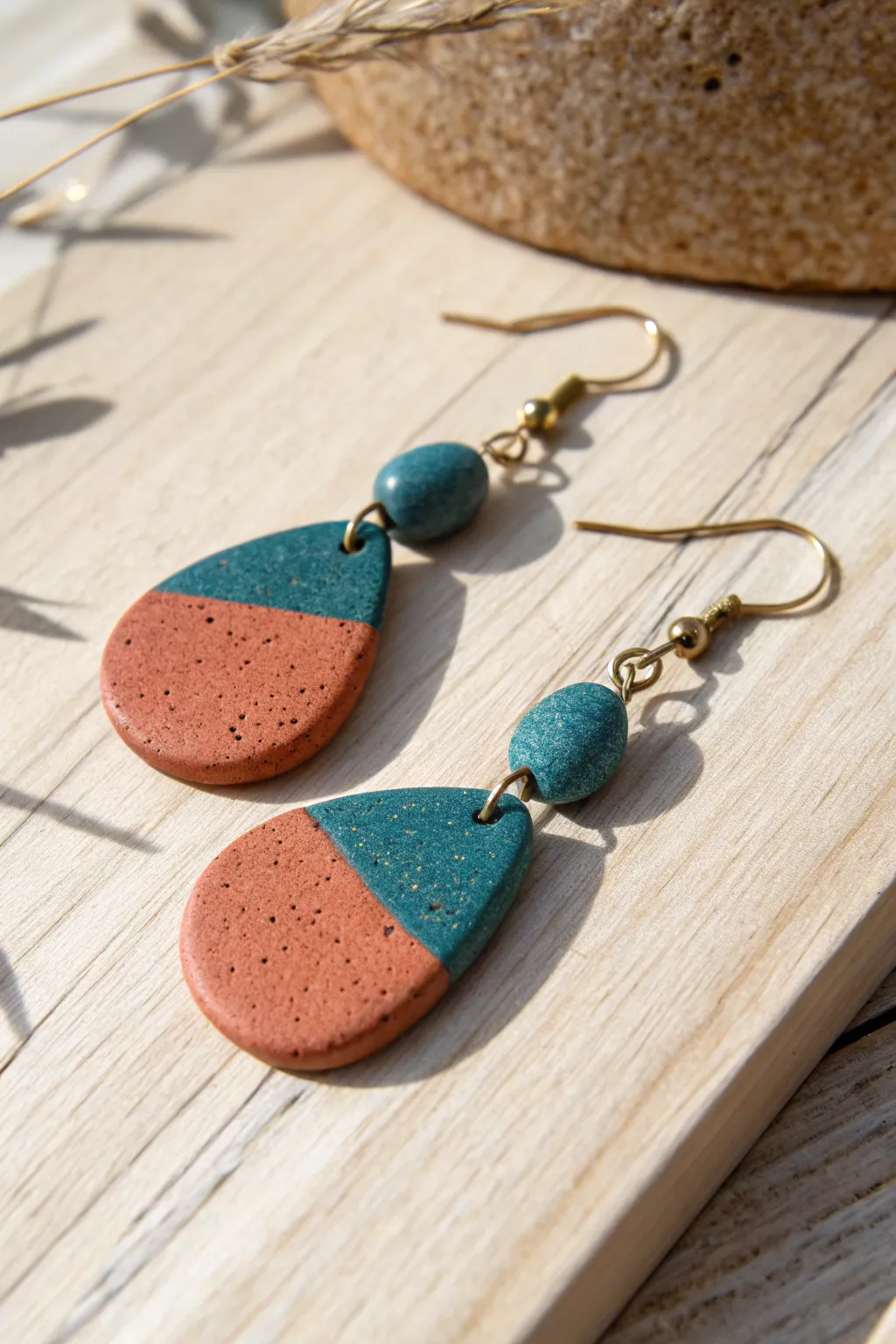 Pebble-shaped polymer clay dangle earrings in bold hues on pale wood, Nordic-boho minimalism.