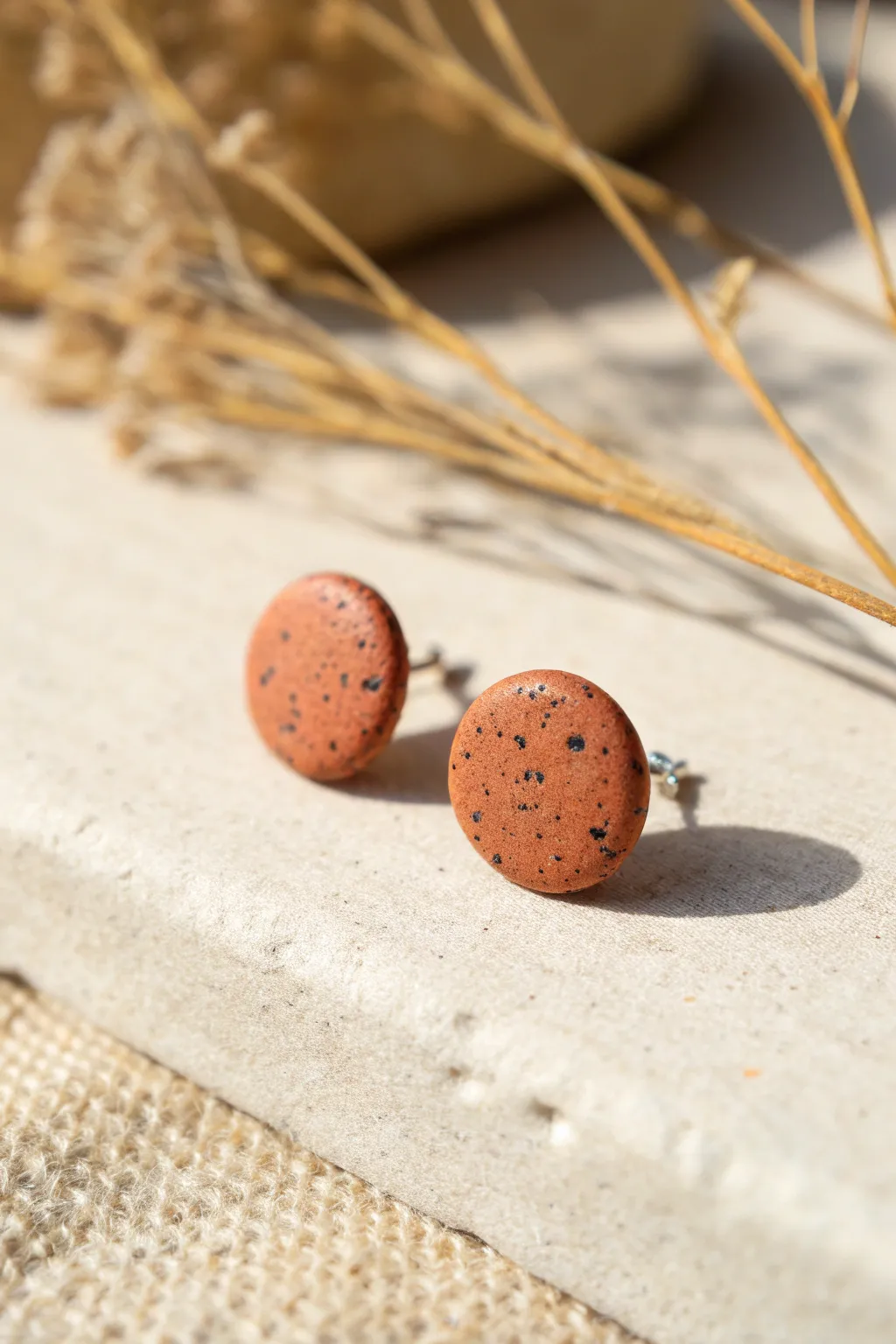 Speckled pebble polymer clay studs in warm terracotta, simple organic shape with bold contrast.