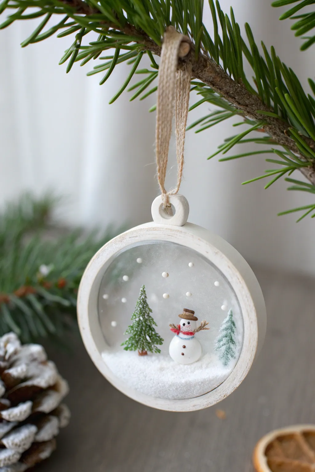 Minimal polymer clay snow globe ornament with a tiny winter scene and soft glowing lights behind.