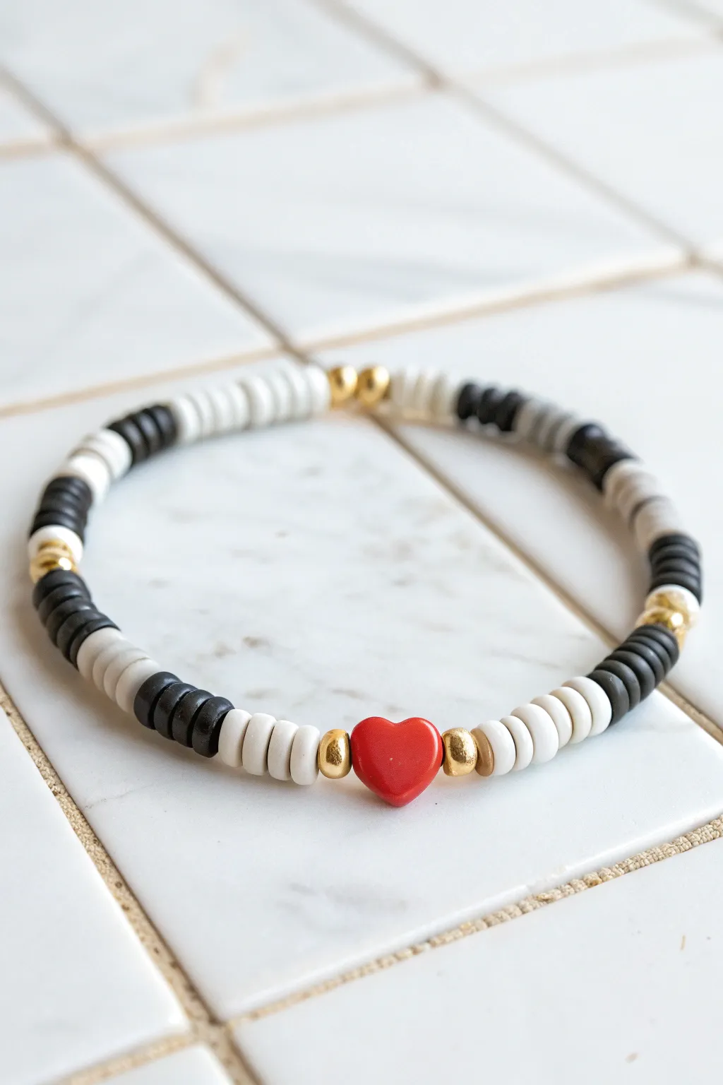 Monochrome heishi bracelet with a bold heart bead and gold spacers, sweet minimalist pop.